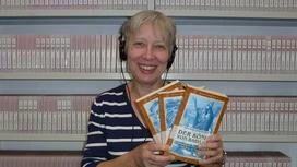 Sigrid Klauß mit drei Büchern in der Hand und Kopfhörer auf dem Kopf
